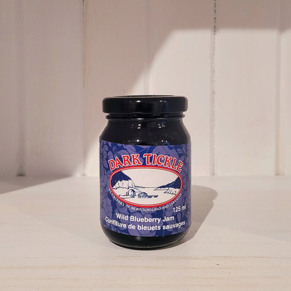 125ml jar of Dark Tickle wild blueberry jam on a white surface with a wooden background
