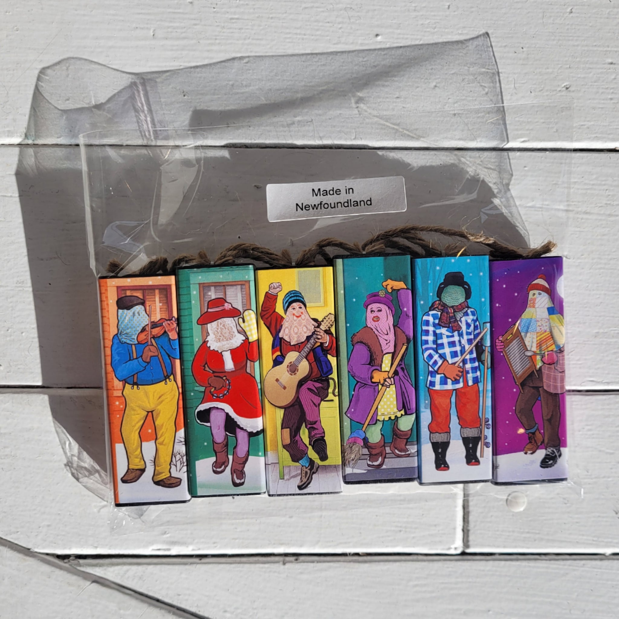 a package of 6 colourful mummer decorations in a clear bag against a white wooden background