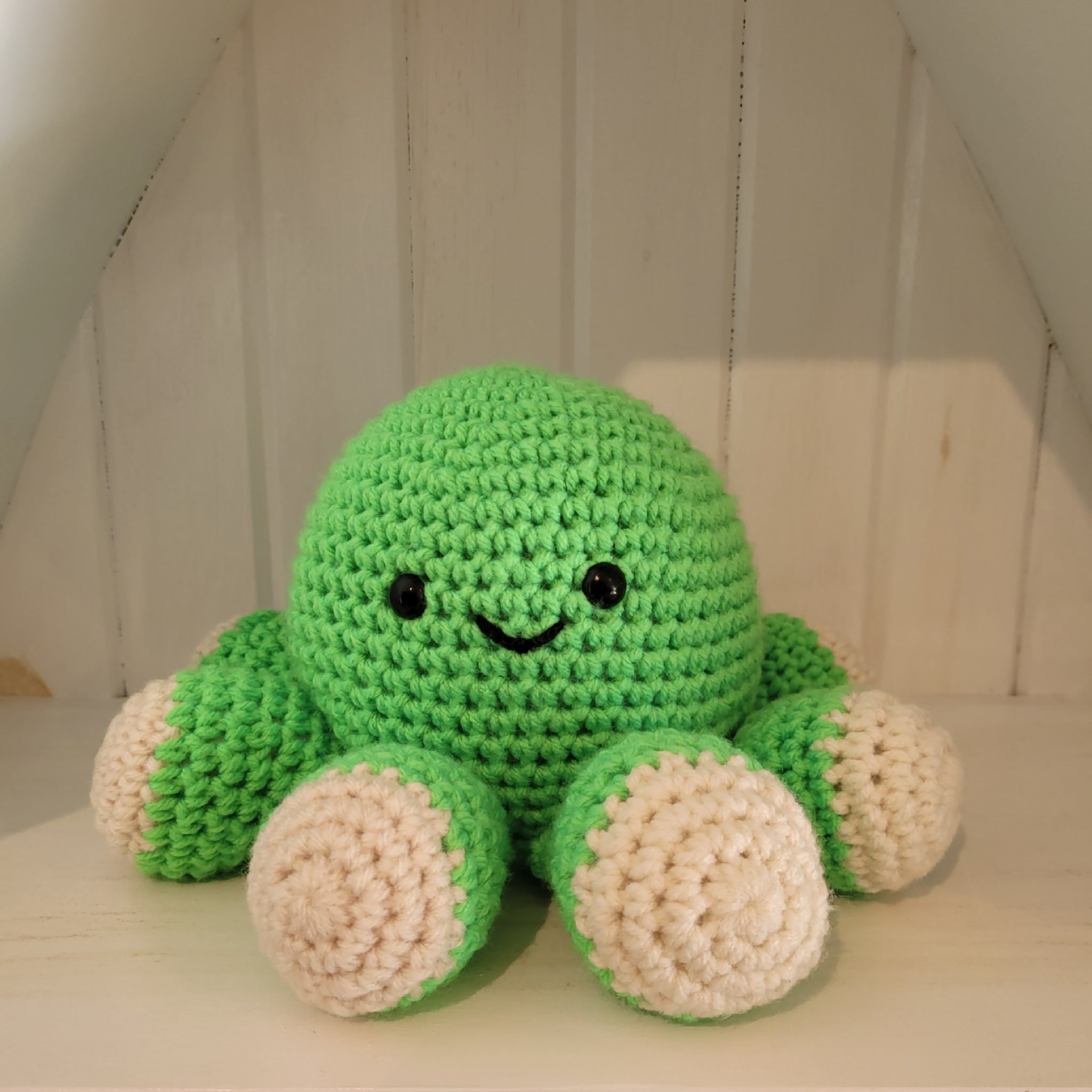 Green crochet octopus plush toy with a smiling face on a white surface against a white background