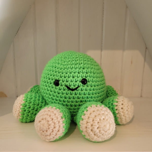 Green crochet octopus plush toy with a smiling face on a white surface against a white background