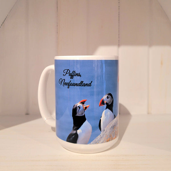 A white mug with panoramic puffin photograph on the side of it and text at the top that says "Puffins, Newfoundland" against white surface