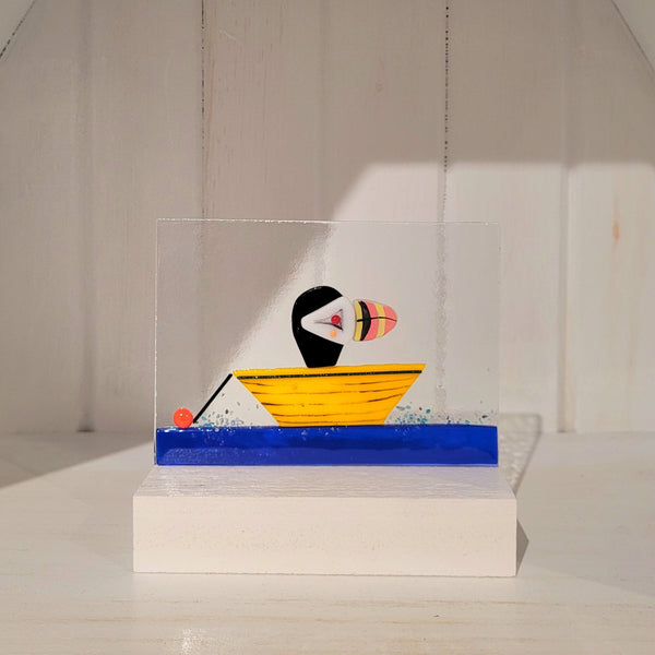 Fused glass puffin in dory on a stand against a white background