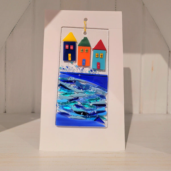 Fused glass plaque of colorful rowhouses near the water against a white background