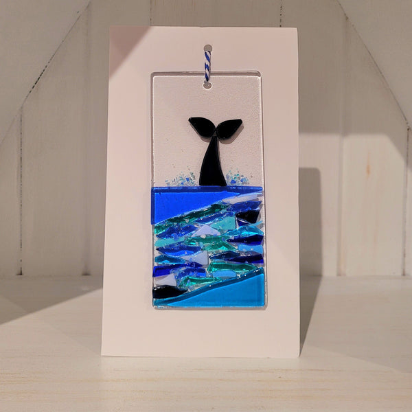 Fused glass whale tail in water on a rectangular plaque against a white background