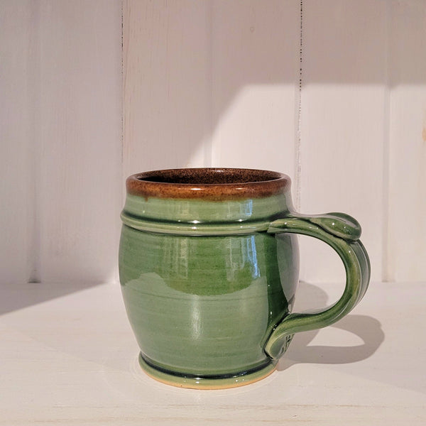 Green ceramic mug with brown rim on a white surface