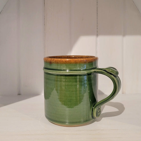 Green ceramic mug with a brown rim on a white surface