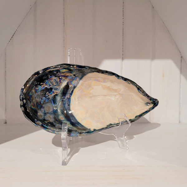 Decorative ceramic dish in the shape of a blue mussel shell on a white stand against a neutral background