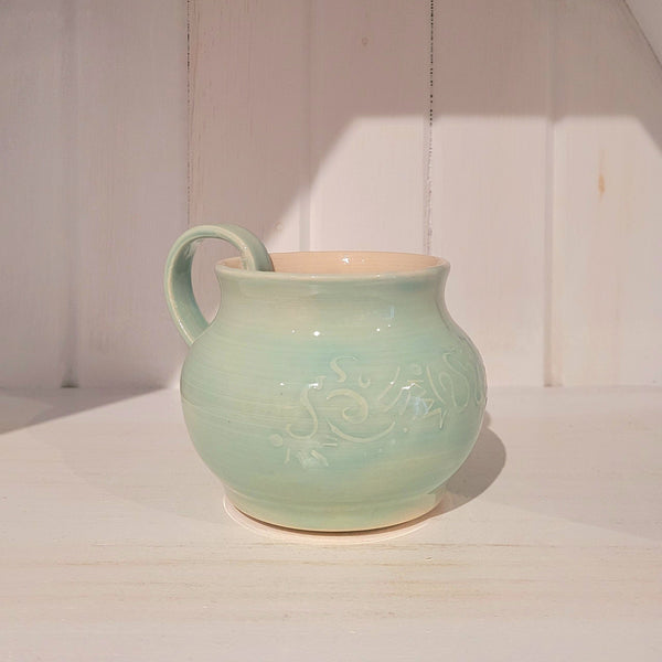 Light green ceramic mug with decorative pattern on a white background
