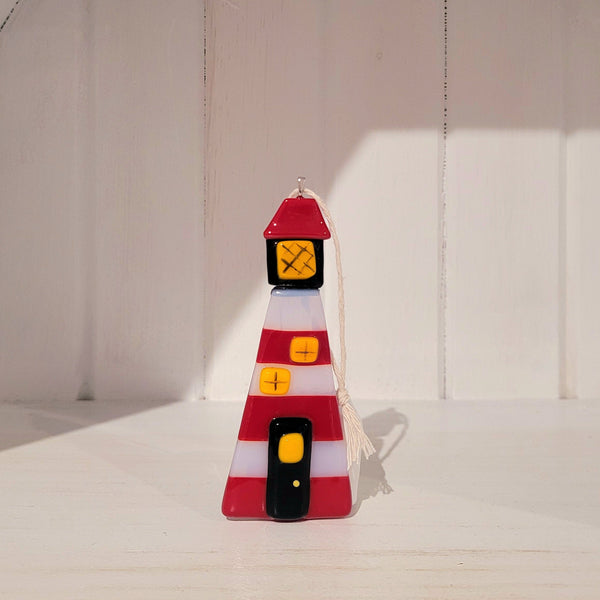 Decorative fused glass lighthouse ornament with red and white stripes on a plain background