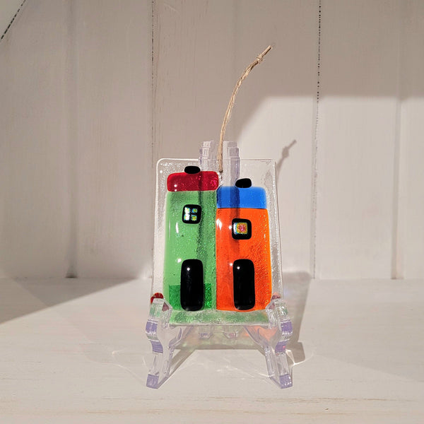 Colorful fused glass rowhouse ornament on a stand against a white background