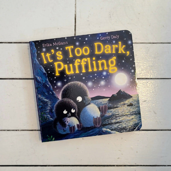 A children's board book titled "It's Too Dark, Puffling" by Erika McCann and Gerry Daly photographed on a white wooden surface.