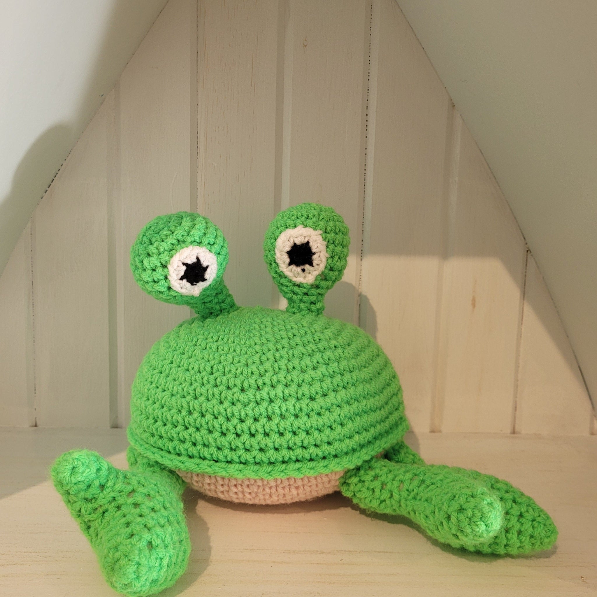 Green crochet crab toy on a wooden surface with a neutral background