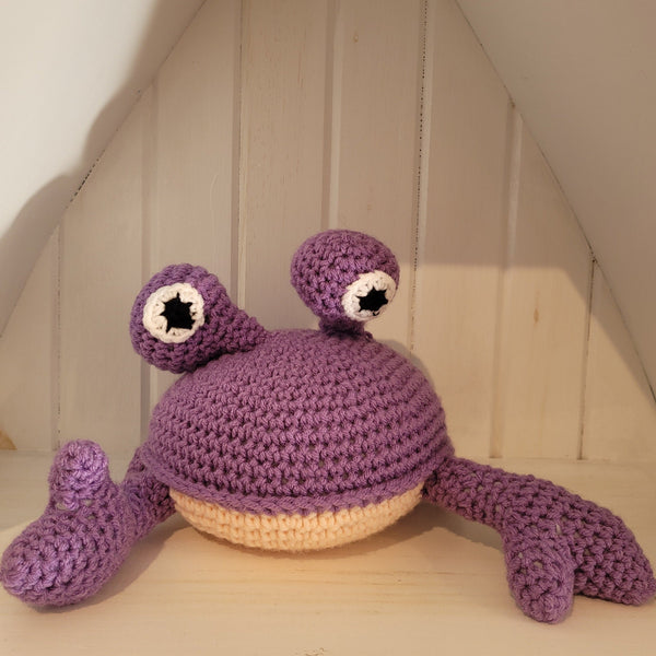 Purple crochet crab toy on a wooden surface with a neutral background