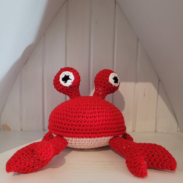 Crocheted red crab toy on a wooden surface with a white wall background