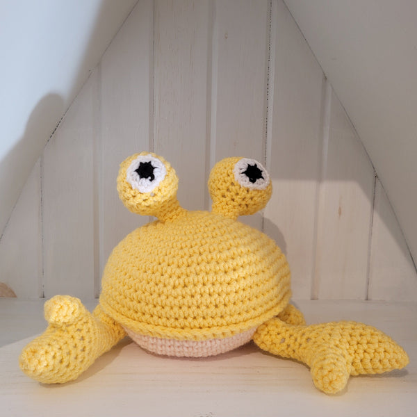 Yellow crochet crab stuffed toy on a white surface against a wooden wall background