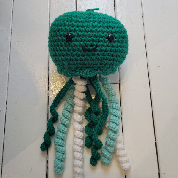 green crochet plush toy jellyfish with smiley face and colourful tentacles on a white background
