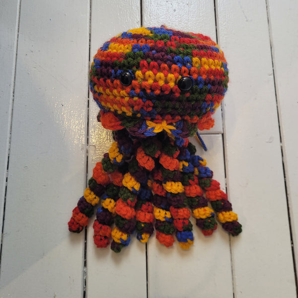 Multicoloured crocheted jellyfish plush toy on a white wooden surface