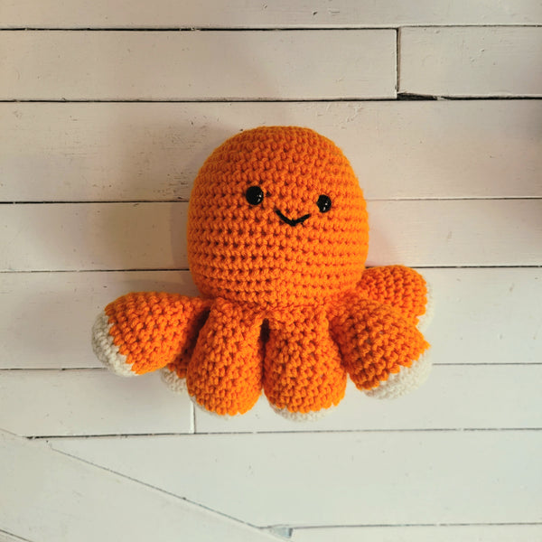 Crocheted orange octopus plush toy on a wooden surface