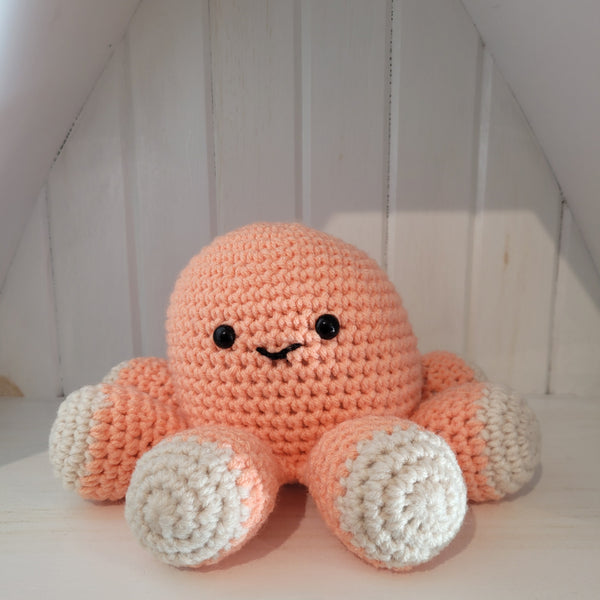 Peach-coloured crocheted octopus plush toy with a smiling face on a white background