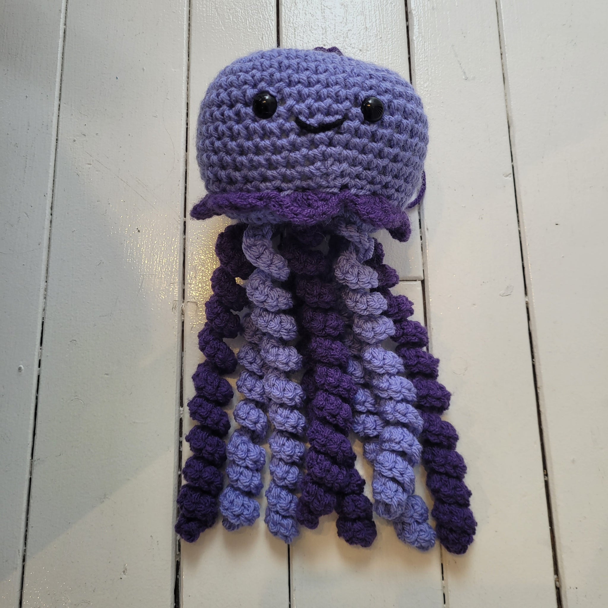 purple crochet plush toy jellyfish with smiley face and colourful tentacles on a white background