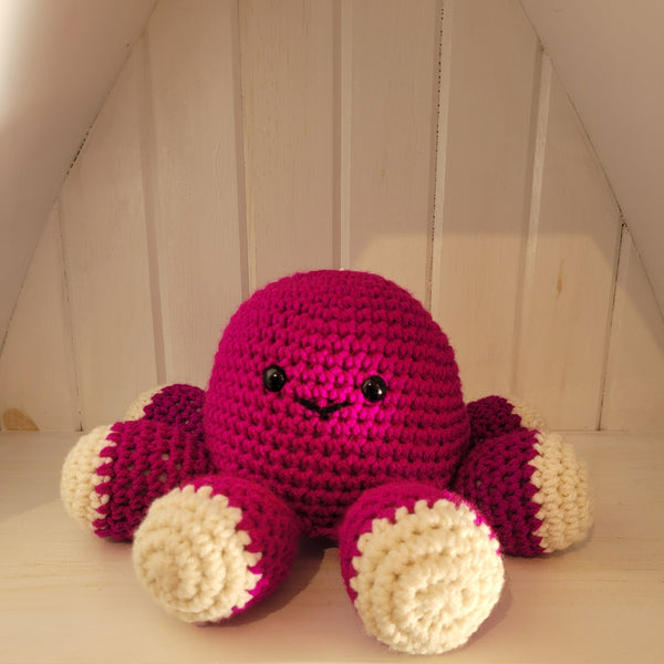 Crocheted purple octopus plush toy on a wooden surface with a neutral background