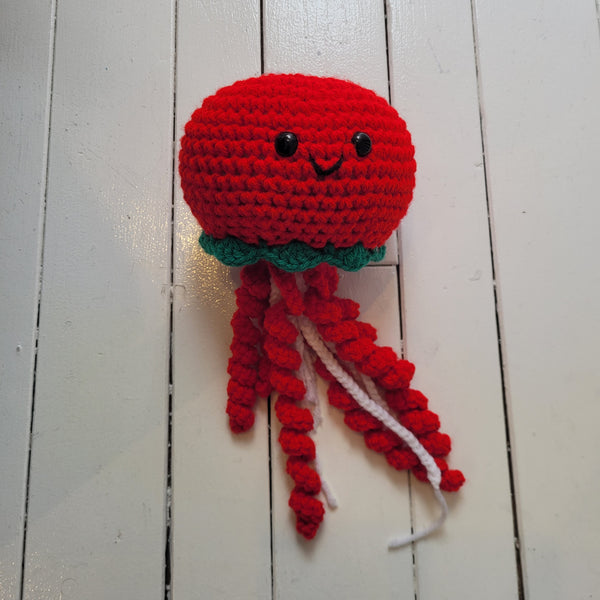Crocheted red jellyfish plush toy on a white wooden surface