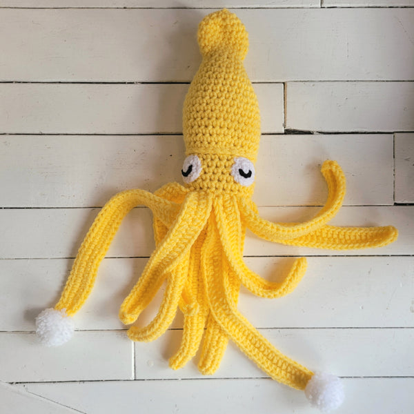 Yellow crochet squid stuffed toy on a wooden surface