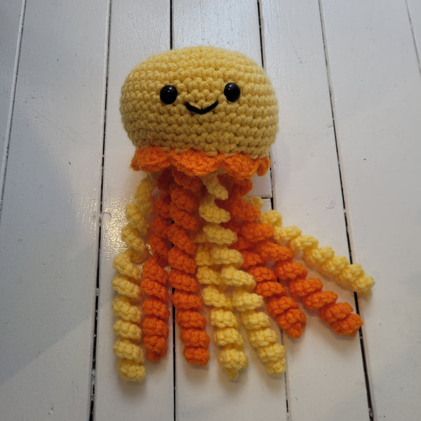 yellow crochet plush toy jellyfish with smiley face and colourful tentacles on a white background