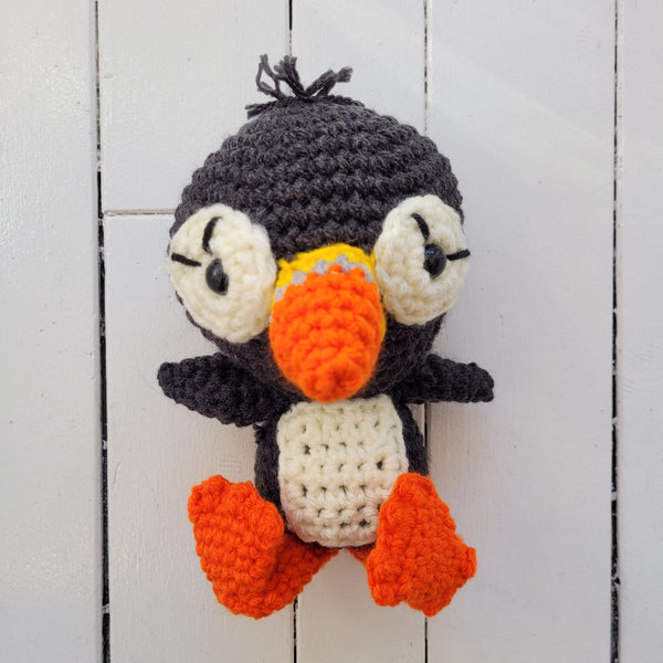 one crocheted plush puffin toy on a white wooden background