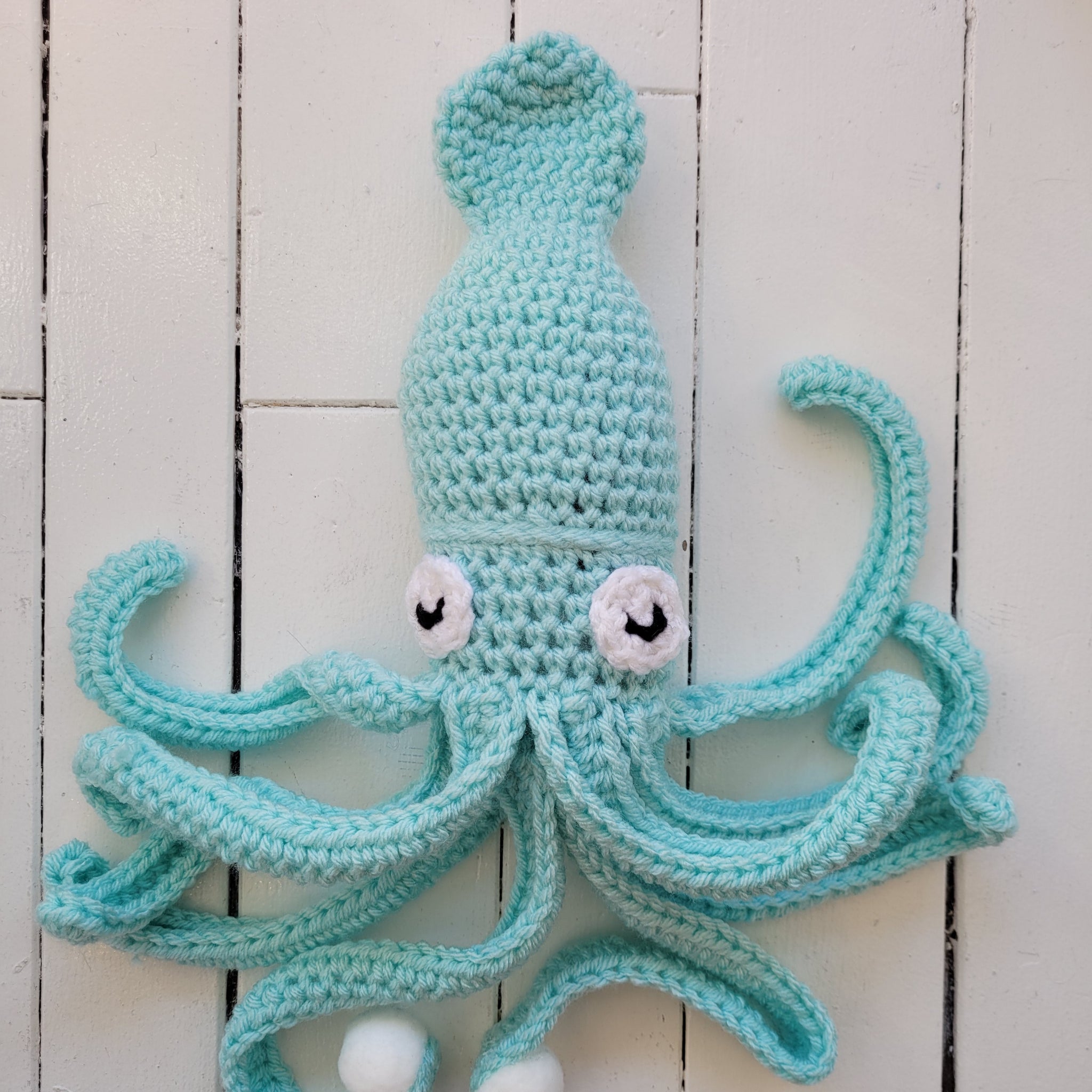 crocheted blue squid on a white wooden background