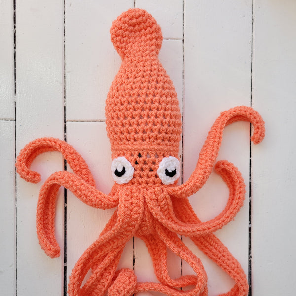 crocheted peach-coloured squid stuffed toy on a white wooden background